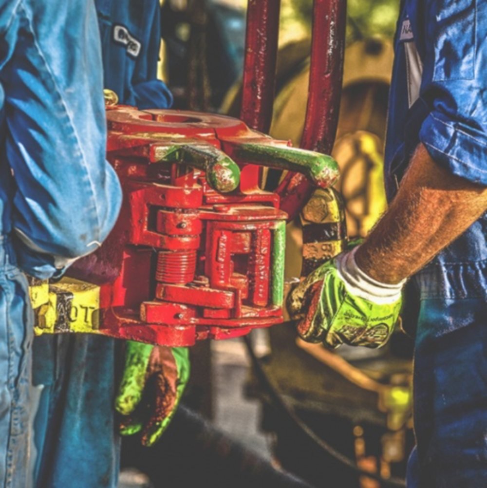 Dos operarios con guantes de protección sujetando una herramienta hidráulica roja en una instalación industrial